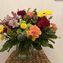 Mixed bouquet in a clear glass vase with roses, lilies, carnations, and daisies