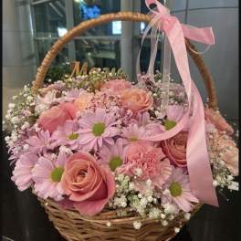 Pink roses and daisies arranged in a wicker basket with a pink ribbon