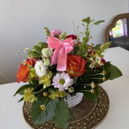 Mixed bouquet of roses, daisies, and alstroemeria in a white basket with a pink bow