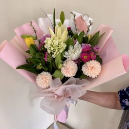Handheld bouquet of mixed pastel flowers wrapped in pink paper