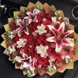 Large bouquet of red and pink roses with white lilies in brown wrap
