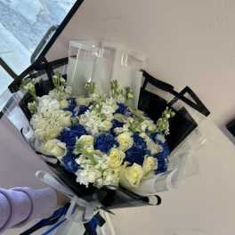 Bouquet of white roses and blue hydrangeas wrapped in black and clear paper