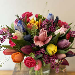 Colorful bouquet of tulips and small purple flowers in a glass vase