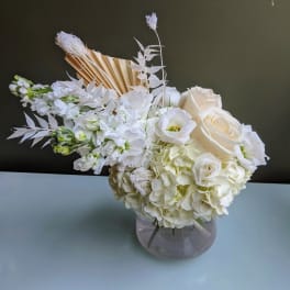 White floral arrangement in a round glass vase with roses and hydrangeas