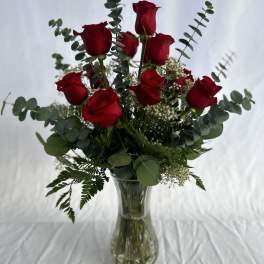 Tall arrangement of red roses with eucalyptus and white filler flowers in a clear glass vase