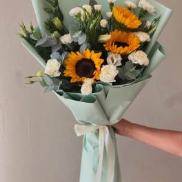 Bouquet of sunflowers and white carnations wrapped in pale mint paper