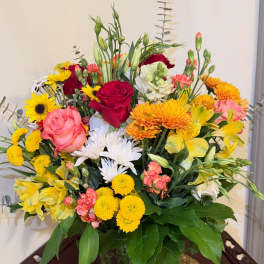 Mixed bouquet of roses, daisies, and yellow blooms in a glass vase