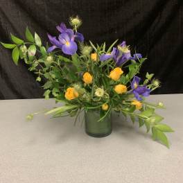 Purple iris and yellow roses arranged in a glass vase