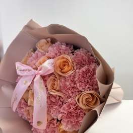 Pink bouquet of carnations and peach roses wrapped in blush paper