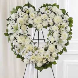 Heart-shaped white floral wreath on a black stand with a white ribbon