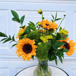 Sunflower arrangement in a clear glass vase with green filler and yellow blooms
