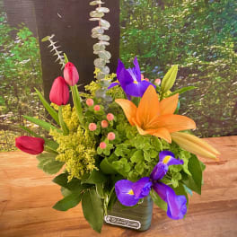 Colorful bouquet with tulips, iris, and lilies in a small vase