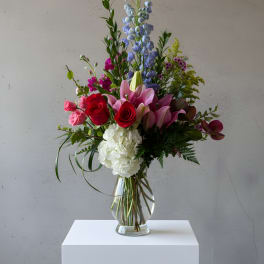 Mixed bouquet with roses, lilies, hydrangea, and blue delphinium in a glass vase