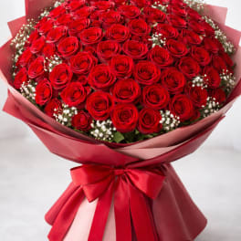 Large bouquet of red roses wrapped in pink paper with a red ribbon
