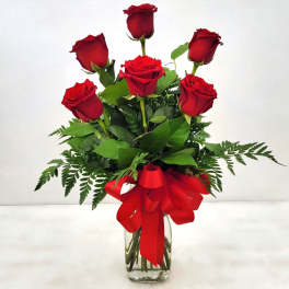 Red roses arranged in a clear glass vase with a red ribbon
