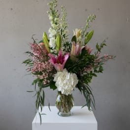 Tall arrangement of pink lilies, white hydrangea, and white stock in a clear glass vase