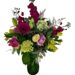 Mixed bouquet of pink, yellow, and green flowers in a glass vase