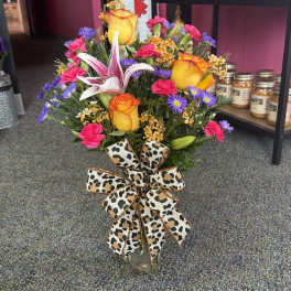 Mixed bouquet with roses, lilies, and a leopard-print bow in a glass vase