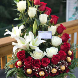 Basket arrangement of red and white roses with white lilies and gold chocolates
