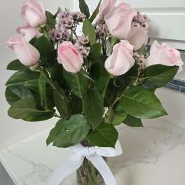Pink roses and small waxflower blooms in a glass vase with a white ribbon.