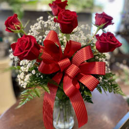Red roses in a glass vase with a large red ribbon and baby's breath
