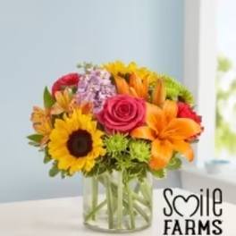 Mixed bouquet in a clear glass vase with sunflowers, roses, and lilies