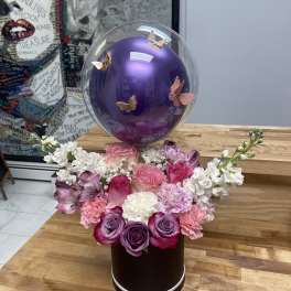 Pink and purple floral arrangement with a clear balloon and butterfly decorations