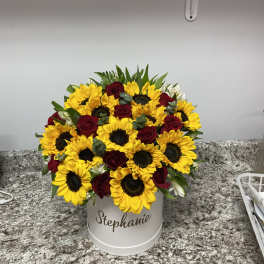 Bouquet of yellow sunflowers and red roses in a white hatbox