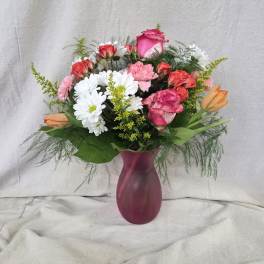 Mixed bouquet of pink roses, white daisies, and orange tulips in a frosted pink vase