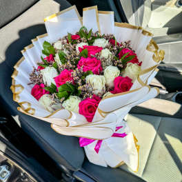 Bouquet of pink and white roses wrapped in white paper with gold trim