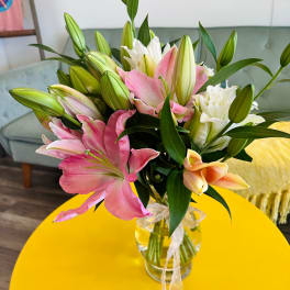 Bouquet of pink, white, and peach lilies with buds in a clear glass vase on a yellow table