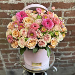 Pink and peach roses and ranunculus arranged in a round pink hat box
