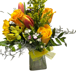Yellow roses and tulips in a clear glass vase with a yellow ribbon