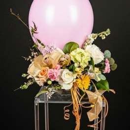 Pink balloon centerpiece with pastel flowers and ribbons in a clear vase on a tall stand