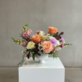 Mixed bouquet of peach, pink, and white flowers in a white vase