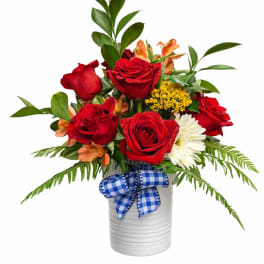 Red roses and mixed flowers in a white vase with a blue check ribbon