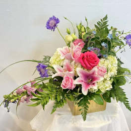 Pink roses and lilies arranged in a wooden container with purple accents