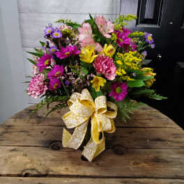 Mixed bouquet of pink, purple, and yellow flowers with a large yellow ribbon