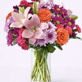 Mixed pink, purple, and orange flowers in a clear glass vase