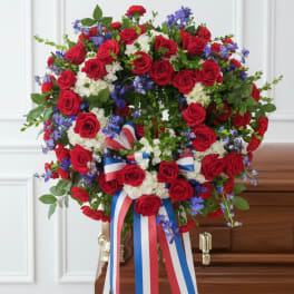 Red rose funeral spray with white flowers and red, white, and blue ribbons