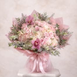 Large round bouquet of pale pink and white roses and hydrangeas with pink orchids, wrapped in pink paper and ribbon
