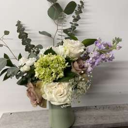 Mixed bouquet of roses, hydrangea, and lavender flowers in a pale green vase