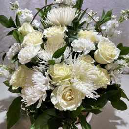 White roses and chrysanthemums arranged in a basket with greenery