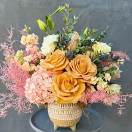 Peach roses and pale pink flowers in a cream vase with pink filler