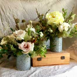 Two floral arrangements in ribbed metal vases with pale roses and yellow blooms
