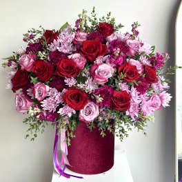 Large arrangement of red and pink roses with pink mums in a dark pink hatbox with ribbon