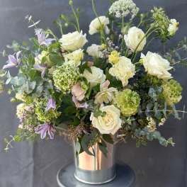 White roses and green blooms in a metal vase with purple flowers