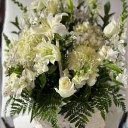 White floral arrangement in a white basket with lilies and roses