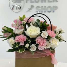 Pink and white flower arrangement in a handled gift box with a ribbon