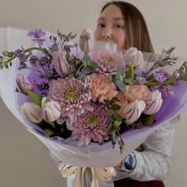 Woman holding a pastel bouquet of tulips and chrysanthemums wrapped in lavender paper